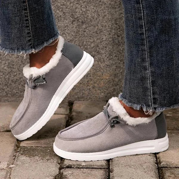Gray winter boots with white fur trim worn with jeans on a stone pavement.
