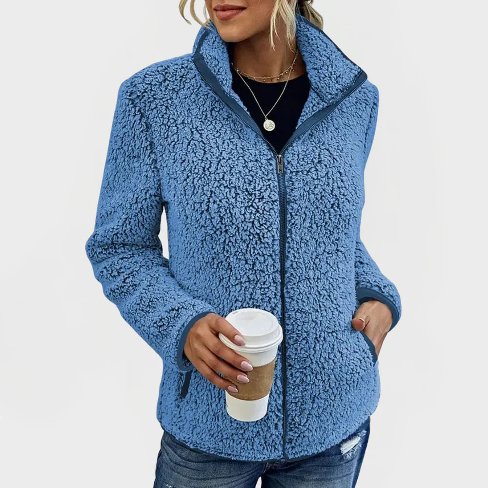 Person wearing a blue sherpa jacket holding a coffee cup on a white background