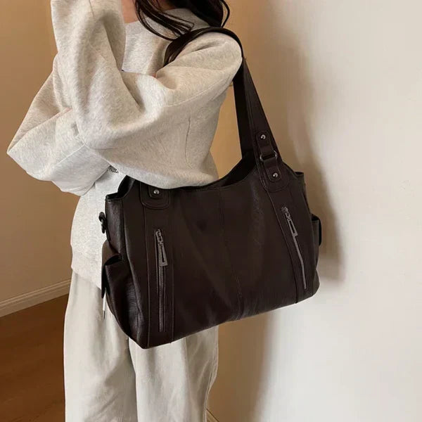 Person wearing a white outfit with a dark brown shoulder bag against a neutral background