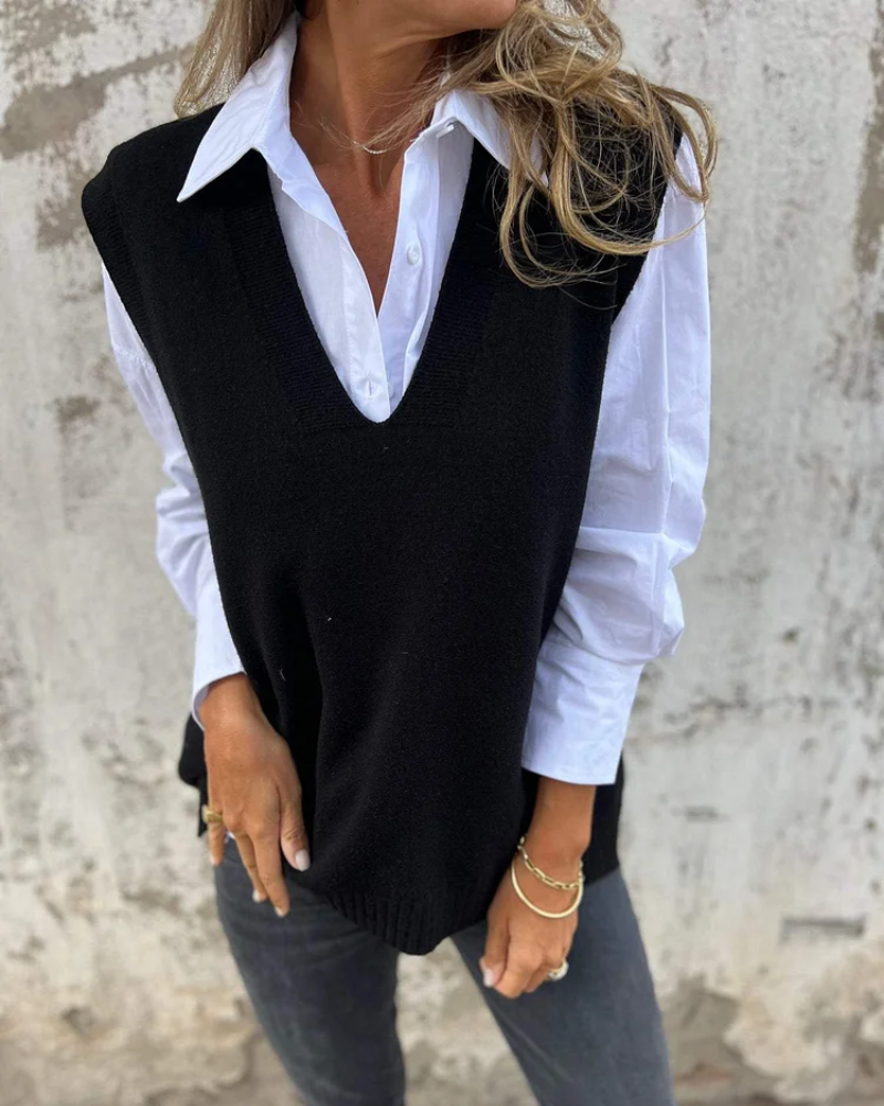 Person wearing a black sweater vest over a white shirt with a neutral background