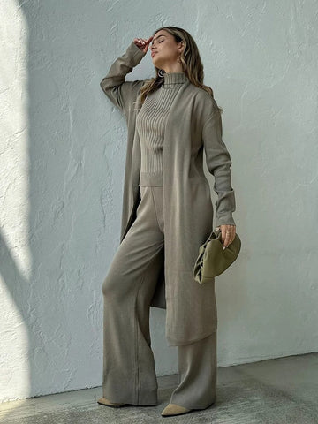 Woman in a beige outfit standing against a light gray wall.