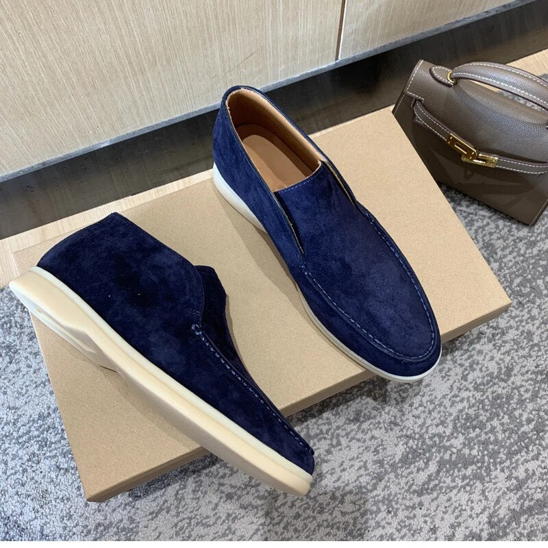Blue suede loafers on a cardboard box with a gray surface and beige wall in the background
