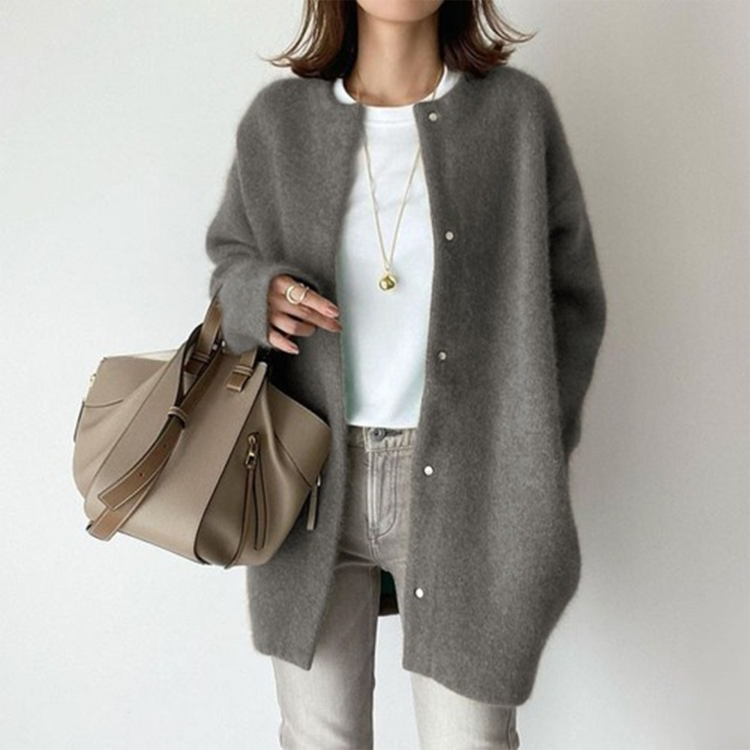 Person wearing a gray cardigan, white shirt, and jeans, holding a beige handbag on a plain background