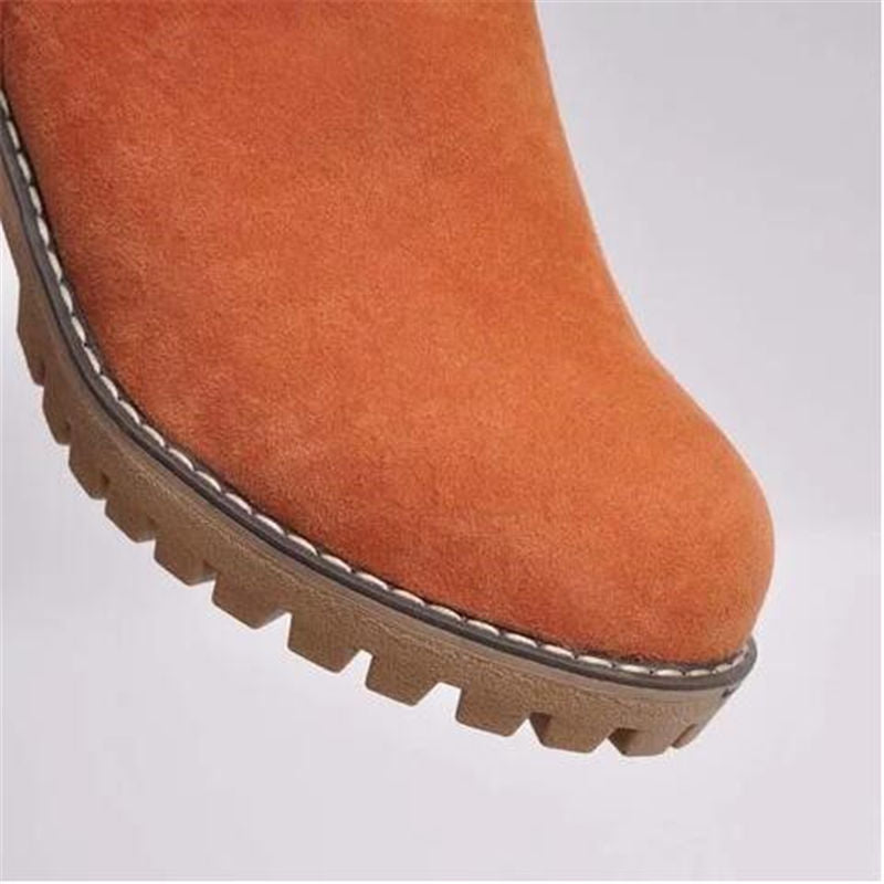 Close-up of a brown suede boot with a textured sole on a light gray background