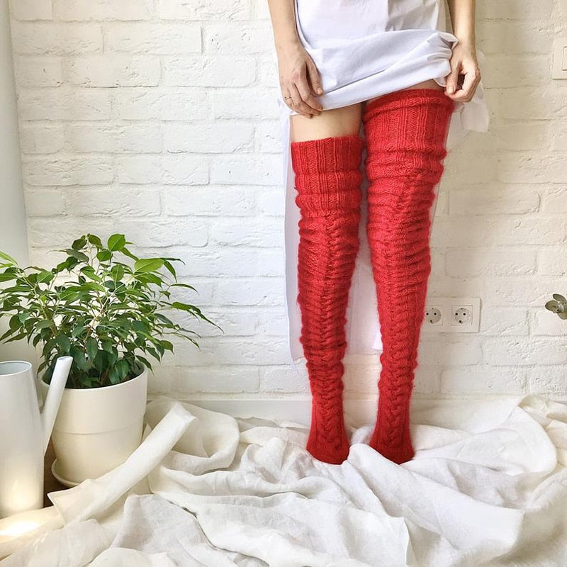 Person wearing red knitted knee-high socks standing on a white blanket with a plant in the background.
