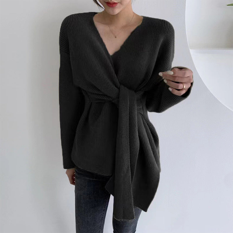 Person wearing a black knitted cardigan with a belt against a white background