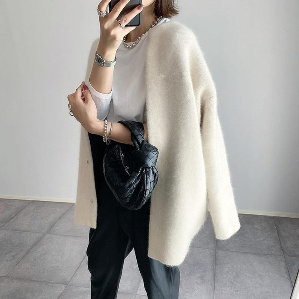Person wearing a beige cardigan over a white shirt and black pants, holding a black bag.