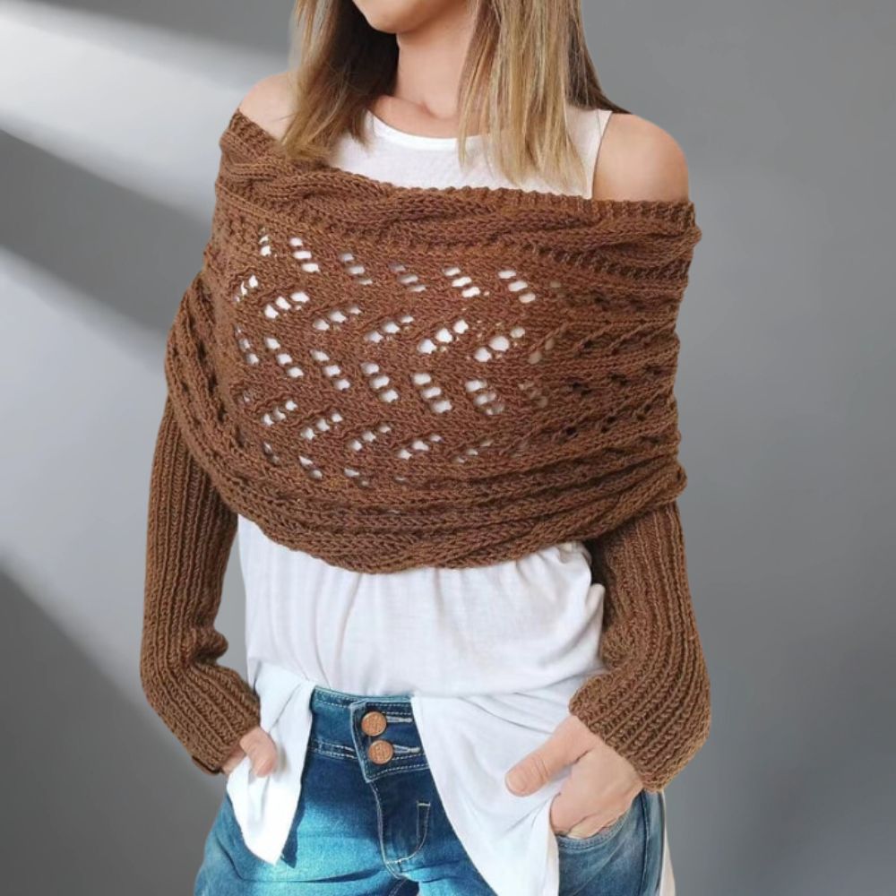 Person wearing a brown knitted shawl over a white top and blue jeans on a gray background