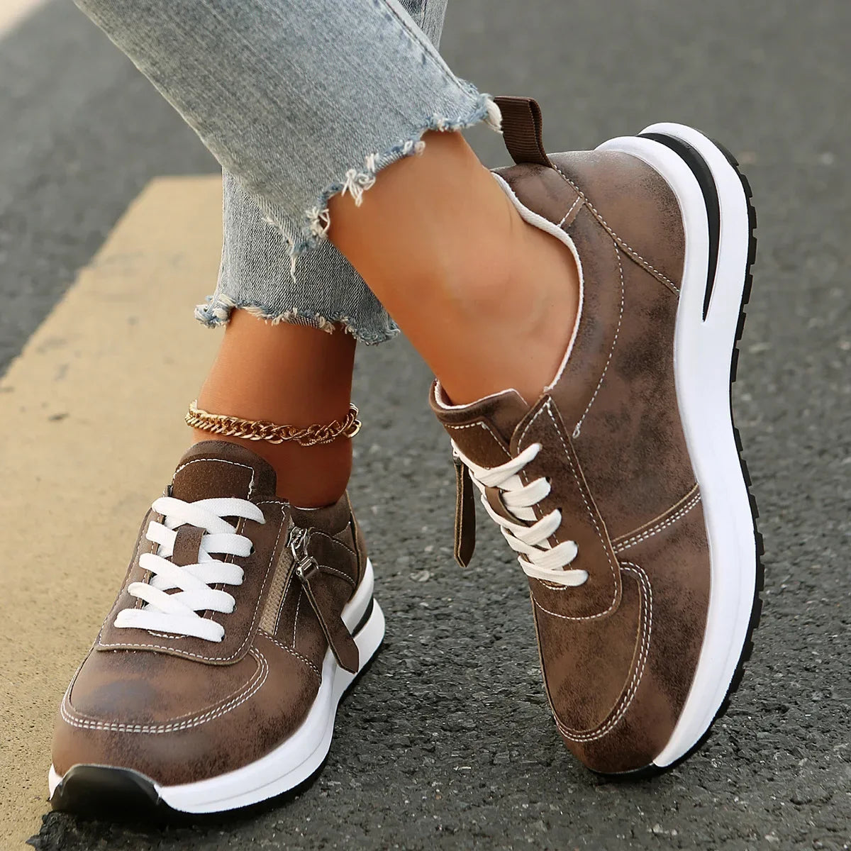 Brown sneakers with white soles worn on a person's feet, standing on a pavement.