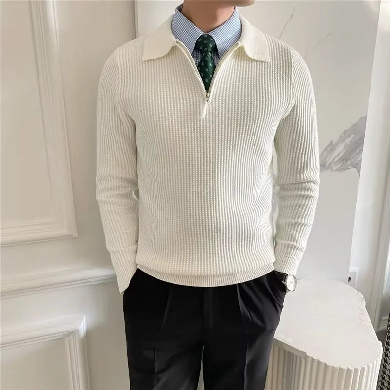 Person wearing a cream sweater over a checkered shirt with a green tie, standing against a neutral background.