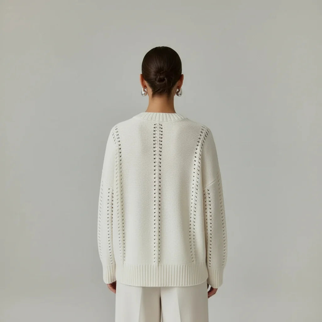Person wearing a white knit sweater with a subtle pattern on a plain background