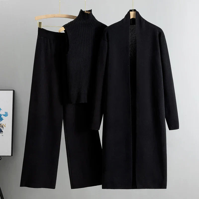 Black coat, black pants, and black shirt on hangers against a gray background