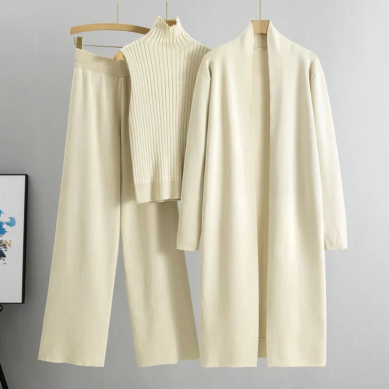 Set of beige clothing items including a cardigan, pants, and a sweater on hangers against a gray background.