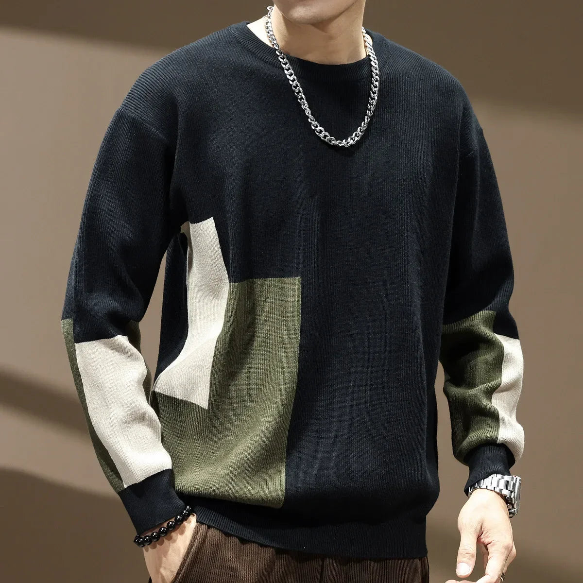 Person wearing a black, green, and white sweater with a chain necklace on a brown background