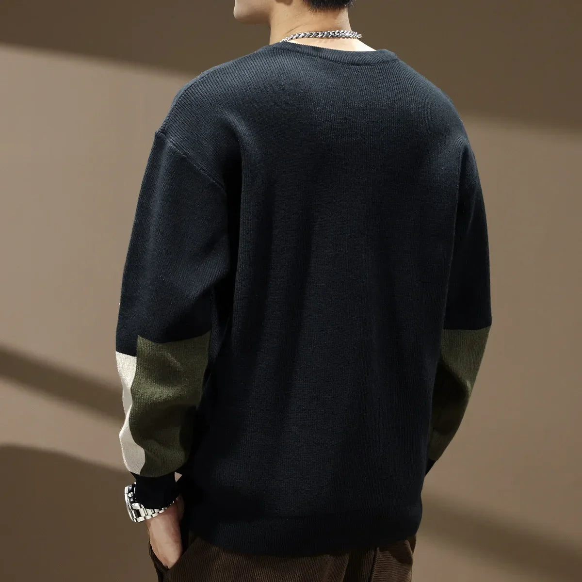 Person wearing a dark sweater with green sleeves against a brown background