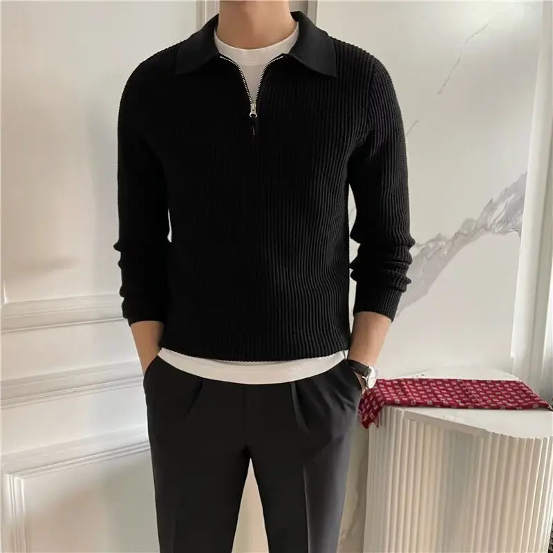 Person wearing a black ribbed sweater over a white shirt with dark pants in an indoor setting.