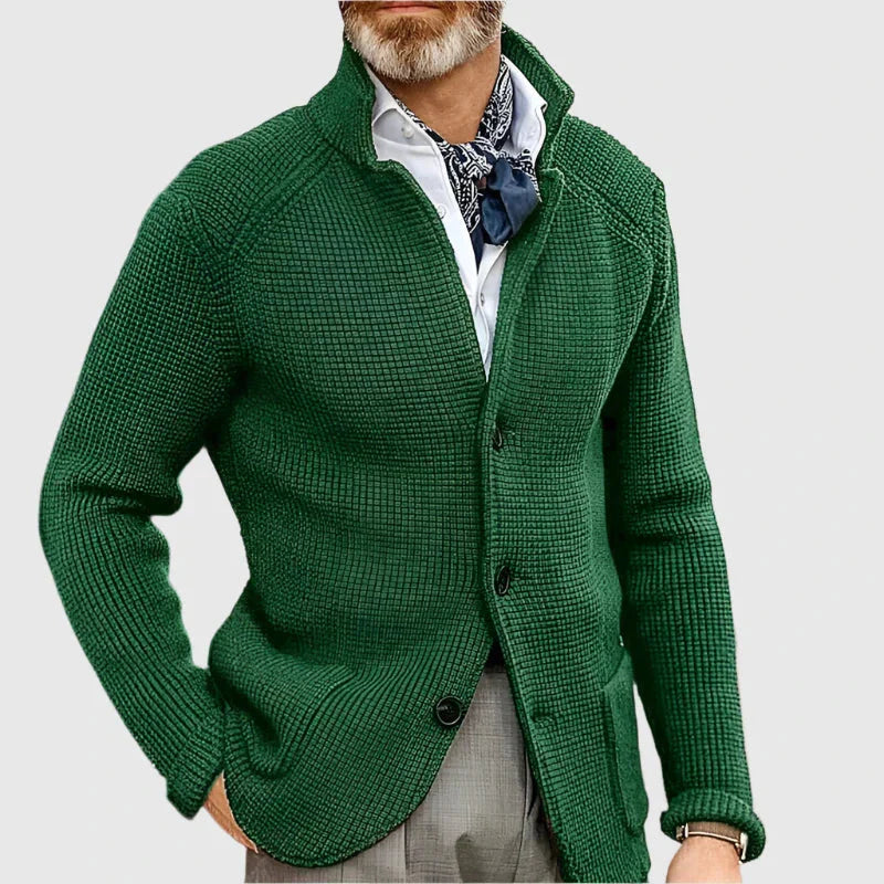 Man wearing a green cardigan over a white shirt with a patterned scarf on a light gray background