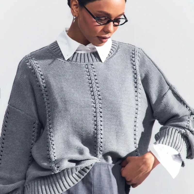 Person wearing a gray knitted sweater over a white shirt on a light background