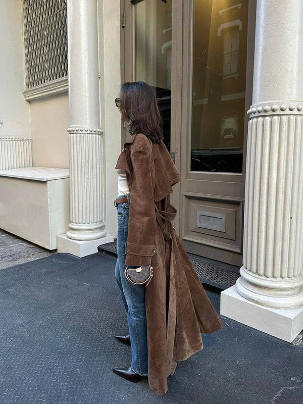 Person wearing a brown coat standing in front of a building entrance.