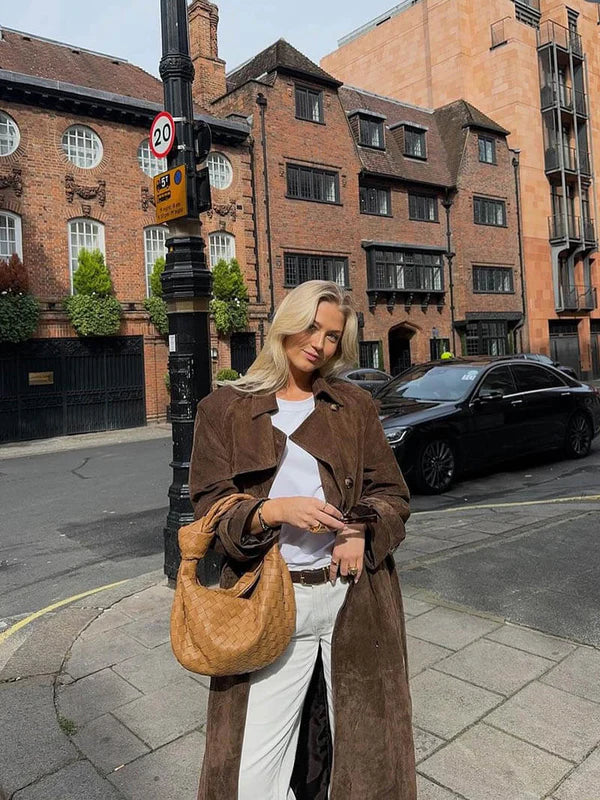 Woman in a brown coat standing on a city street with brick buildings in the background
