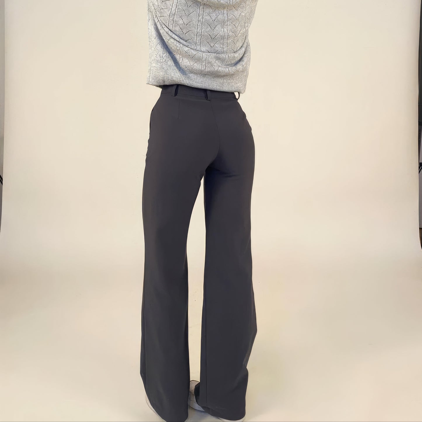 Person wearing dark gray pants and a light gray sweater on a plain background