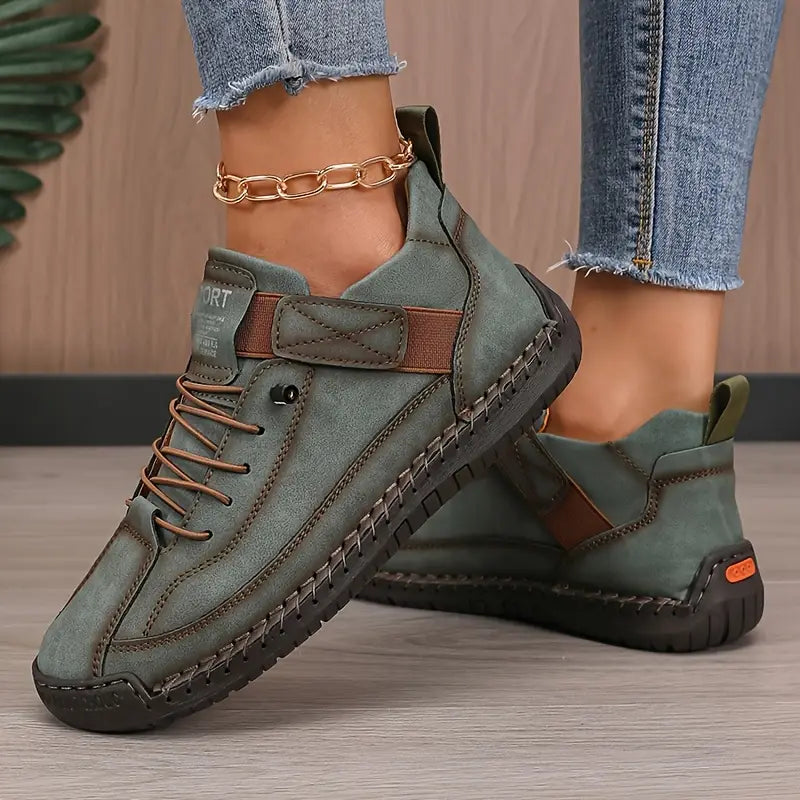 Green boots with brown accents worn by a person on a wooden floor.