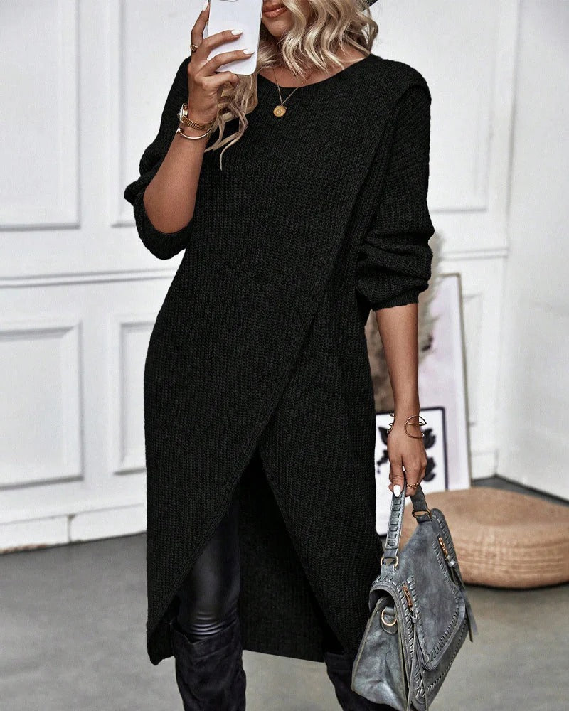 Person wearing a black long-sleeve dress holding a gray handbag indoors.