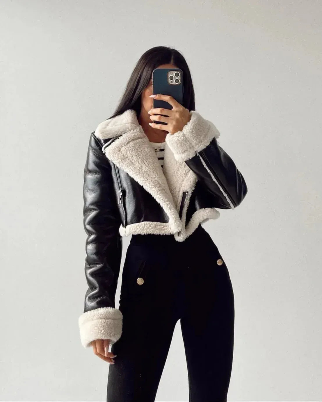 Person wearing a black leather jacket with white fur trim against a plain background