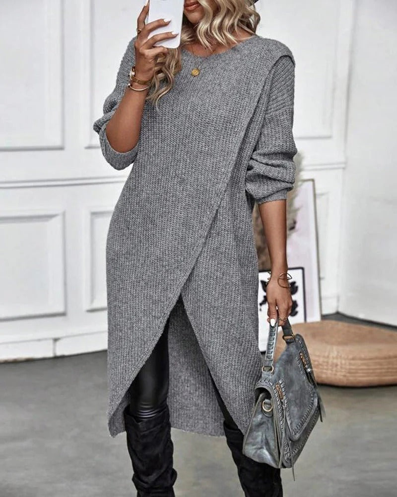 Person wearing a long gray sweater with a white wall background
