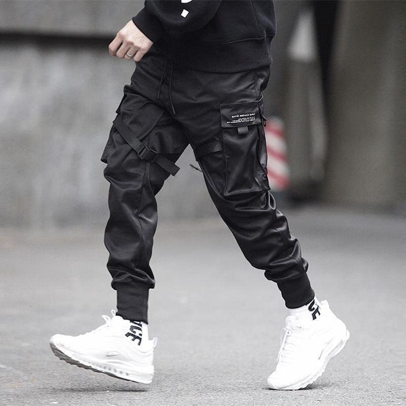 Person wearing black cargo pants and white sneakers on a blurred street background