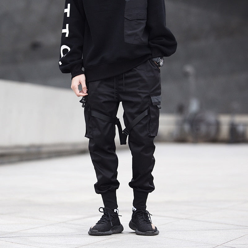Person wearing black cargo pants and a black sweatshirt with white text, standing on a concrete surface.