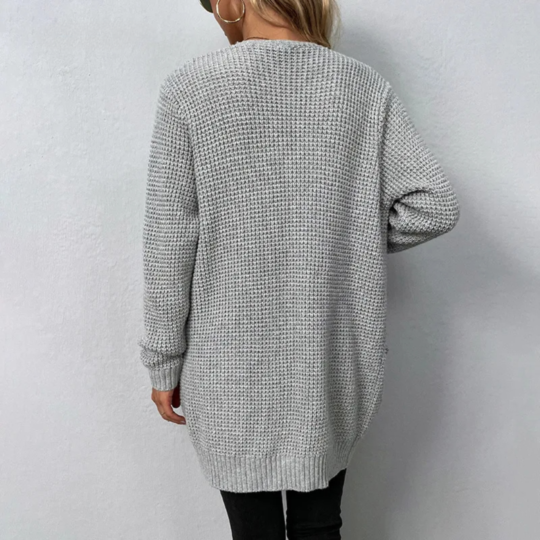 Person wearing a long gray knitted cardigan against a plain background