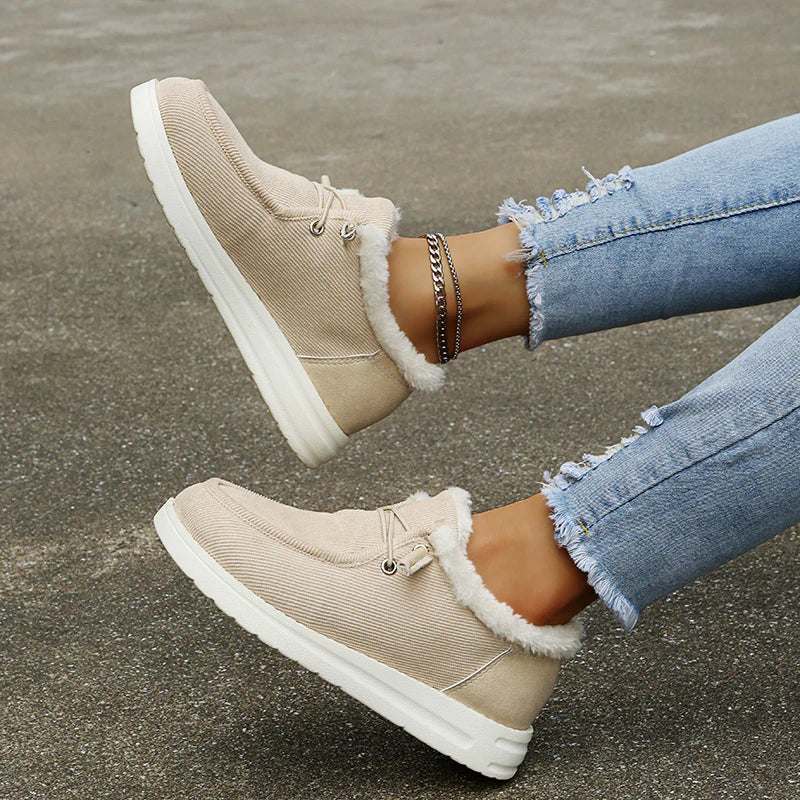 Beige winter boots with white fur lining worn by a person on a concrete surface.