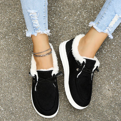 Black sneakers with white soles and fur trim worn with light blue jeans on a concrete surface.