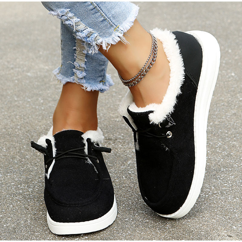 Black sneakers with white fur lining worn by a person on a concrete surface