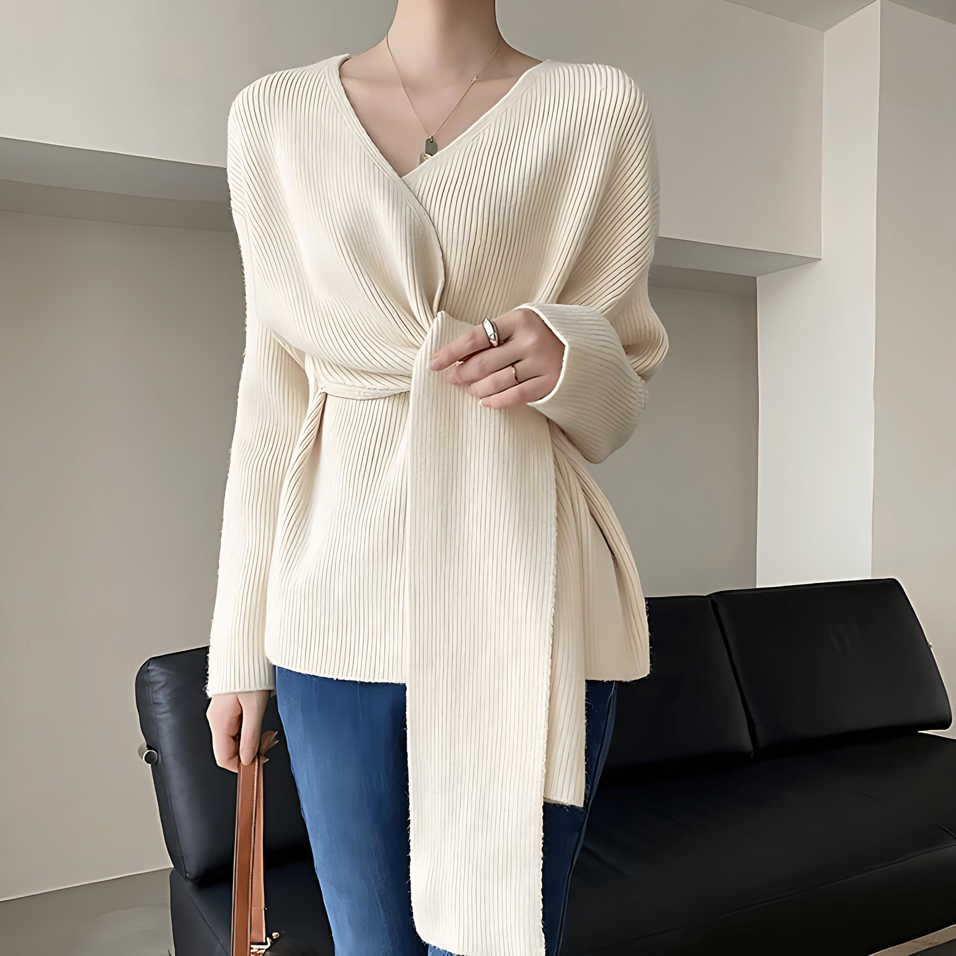 Mannequin wearing a cream ribbed sweater with a black sofa in the background