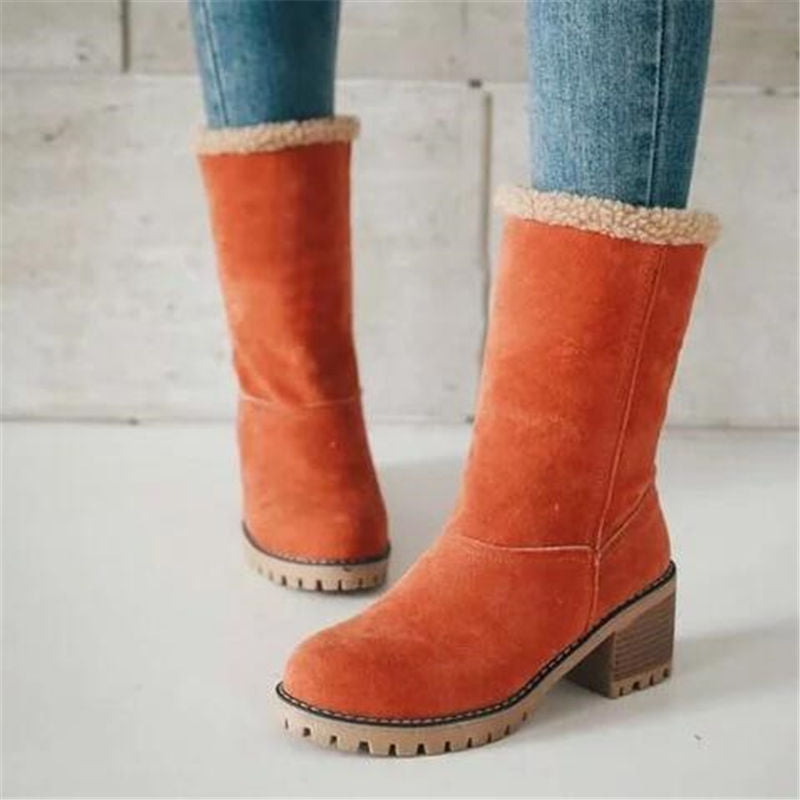 Orange suede boots with beige lining worn with blue jeans on a light wooden floor.