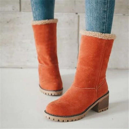 Orange suede boots with beige lining worn with blue jeans on a light wooden floor.