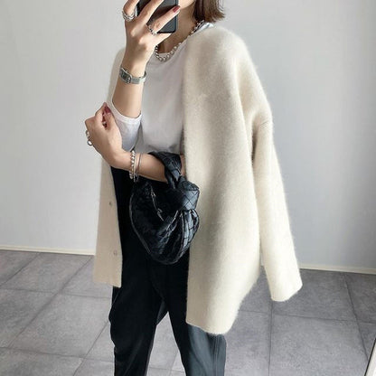 Person wearing a beige cardigan over a white shirt and black pants, holding a black bag.