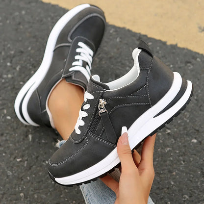 Black sneakers with white laces and sole held by a hand on a pavement background
