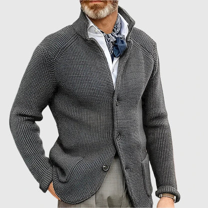 Man wearing a gray textured jacket with a white shirt and patterned scarf on a light gray background