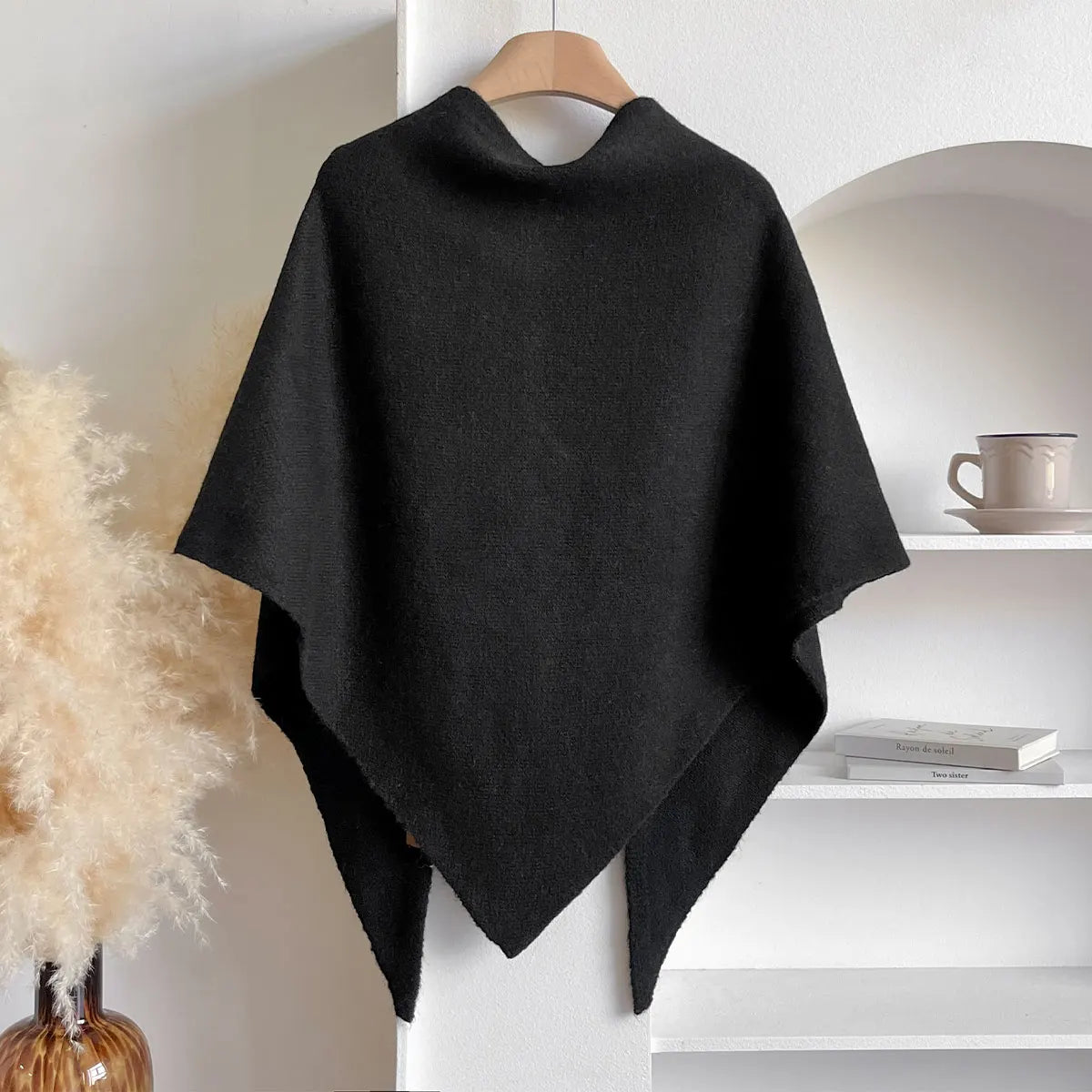 Black poncho on a hanger against a neutral background