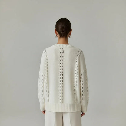 Person wearing a white knit sweater with a subtle pattern on a plain background