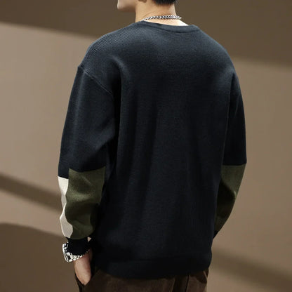 Person wearing a dark sweater with green sleeves against a brown background
