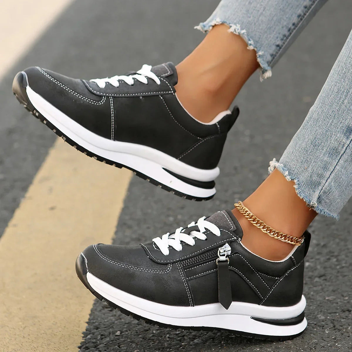 Black sneakers with white soles worn on a person's feet, standing on a pavement.