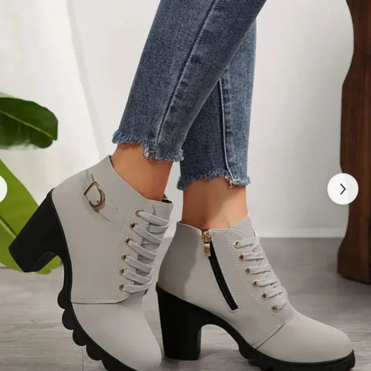 White ankle boots with black soles worn with blue jeans on a light background