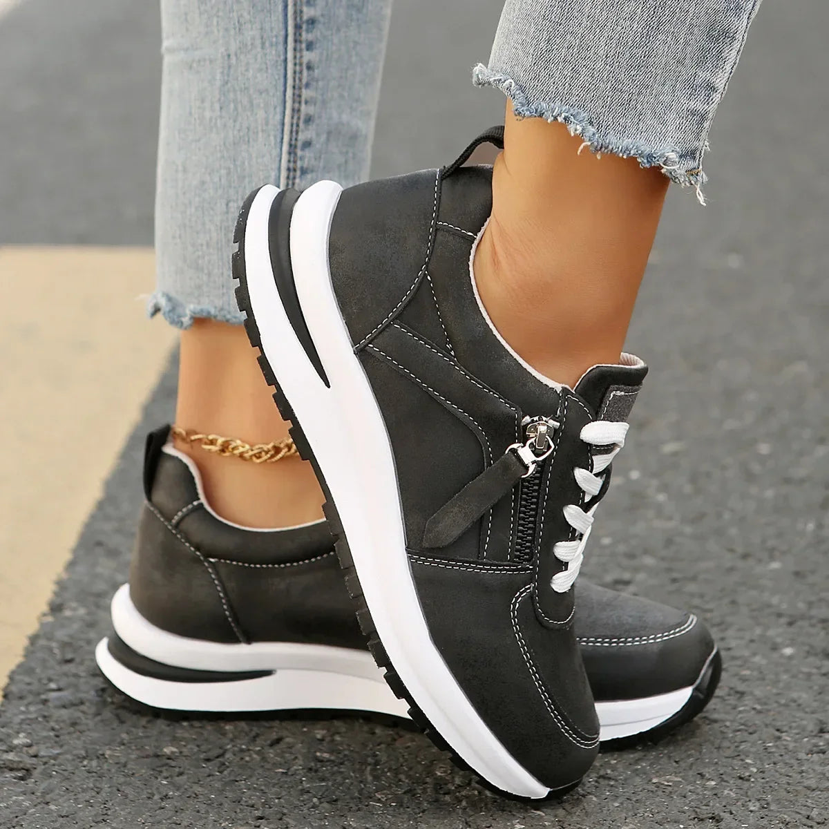 Black sneakers with white soles worn on a street, paired with light blue jeans.