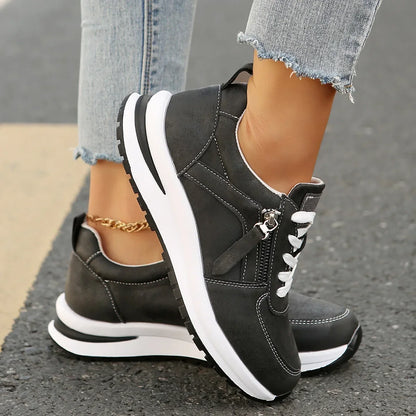 Black sneakers with white soles worn on a street, paired with light blue jeans.
