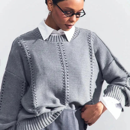 Person wearing a gray knitted sweater over a white shirt on a light background