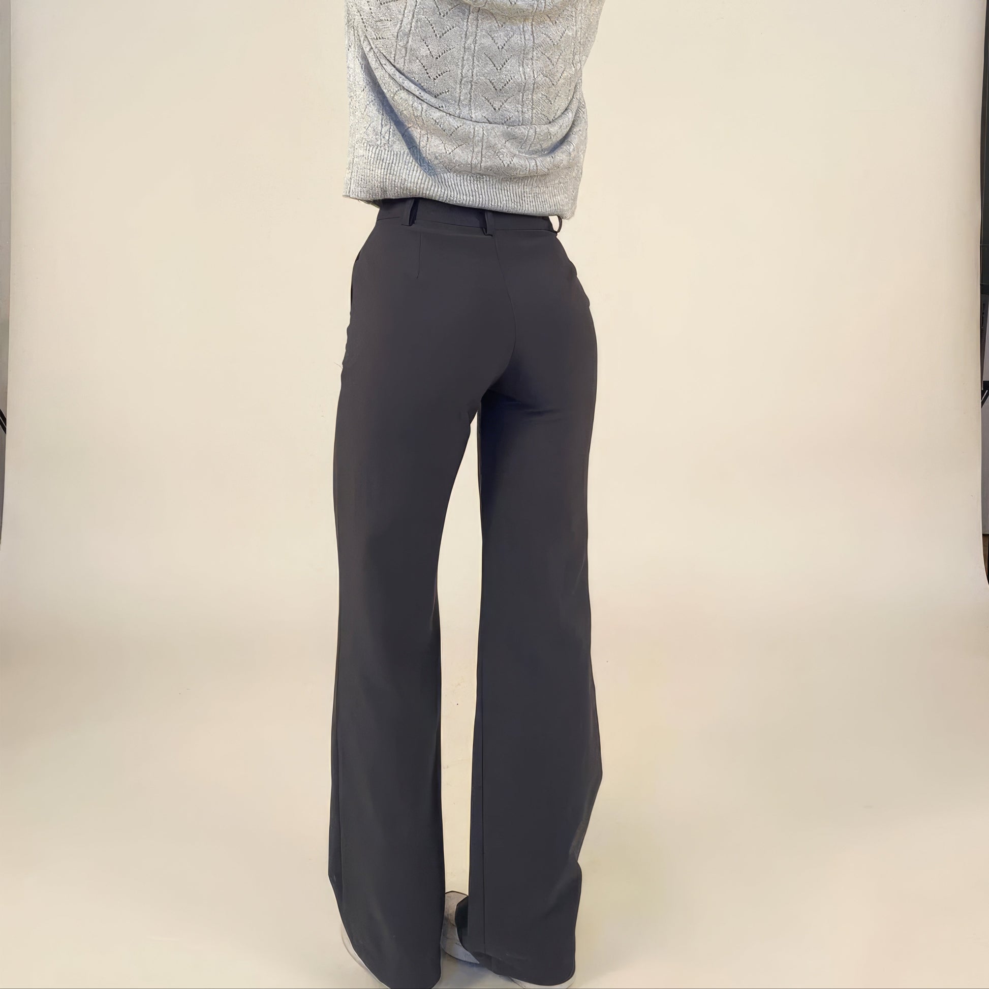 Person wearing dark gray pants and a light gray sweater on a plain background